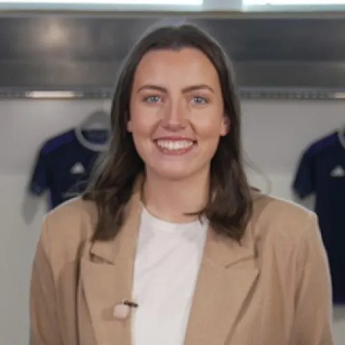 Amy Canavan, 30 under 30 nominee in 2023 smiling at the camera with football jerseys in background.