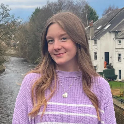 Ellie Craig, 30 under 30 nominee in 2023 smiling at the camera with water and houses in background.