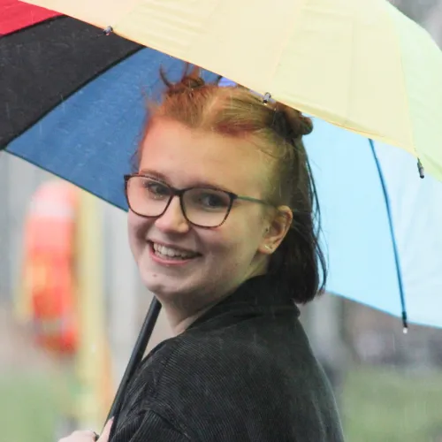 Emma Prach, 30 under 30 nominee in 2023 holding an umbrella in her hand smiling at the camera.