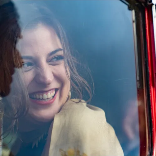 Gabrielle Blackburn smiling from inside of a car through window looking off at camera.