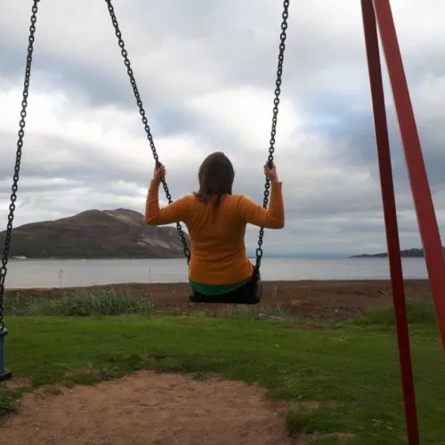 A photo of Jenny on a swing, with a body of water in the background