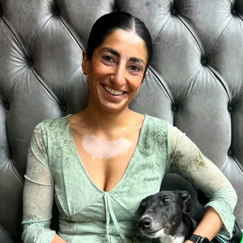Nakita Kaur, 30 under 30 nominee in 2023 holding a dog in her hands smiling at the camera.