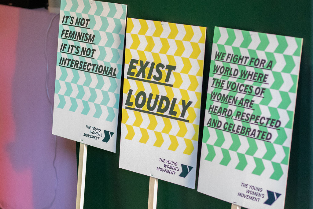 Placards that say 'It's not feminism if it's not intersectional', 'Exist loudly' and 'We fight for a world where the voices of young women are heard, respected and celebrated.'