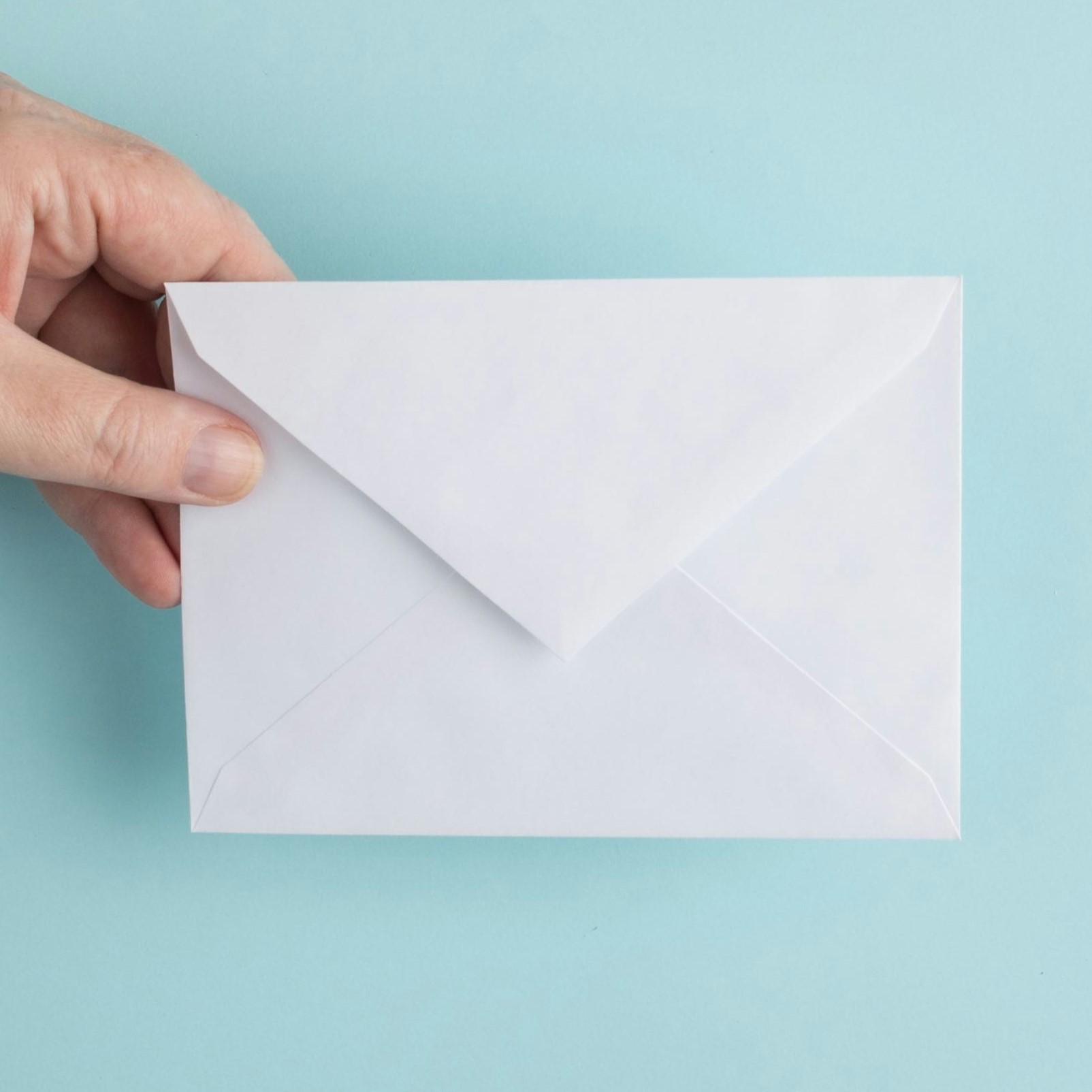 Hand holding an envelope against a pale blue background